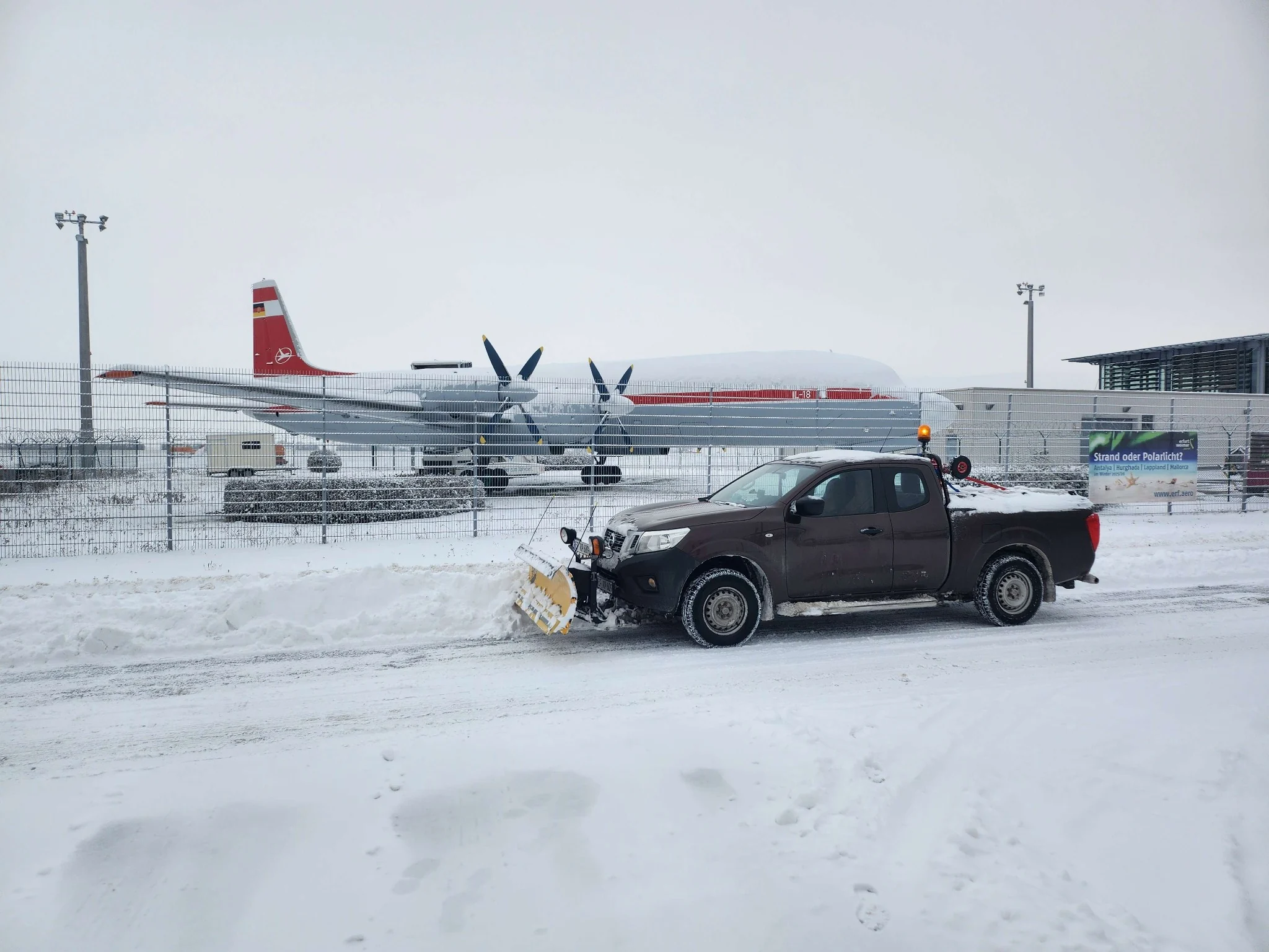 Eigenes Winterdienstfahrzeug mit Schneeschild vor einem Flughafengelände